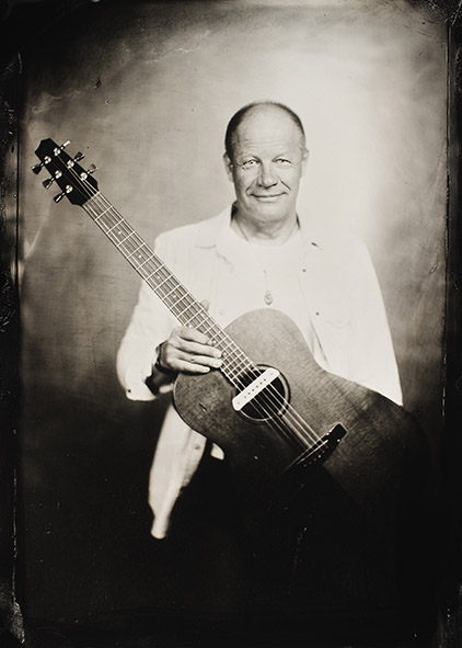 Mustavalkoinen kuva miehestä kitara kädessä.